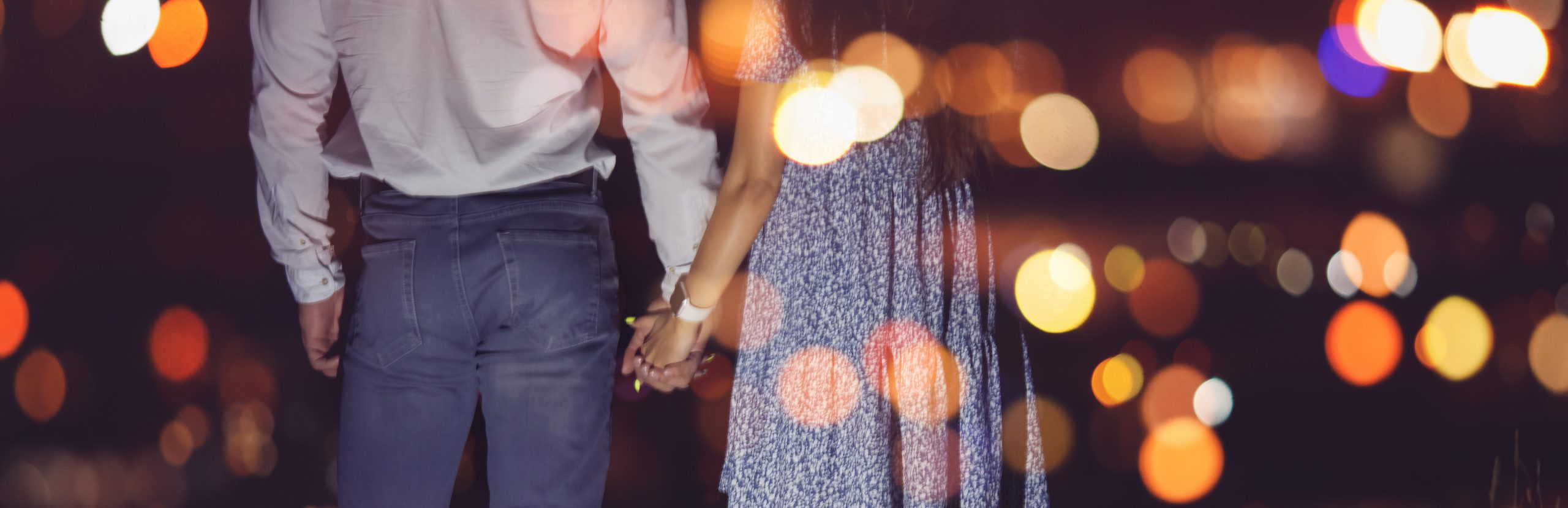 Romantic couple in love holds hands against backdrop of night city lights