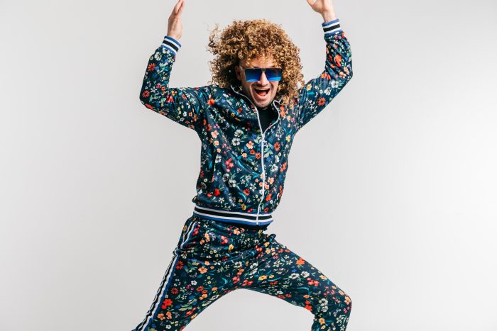 Excited adult funny man in stylish vintage clothes posing on white studio background. 80s fashion. Funky guy in tracksuit and sunglasses expressive indoor unusual portrait. Shouting cheerful male.