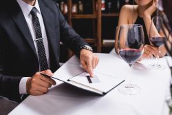 Cropped view of man putting credit card in restaurant bill near glasses of wine and girlfriend